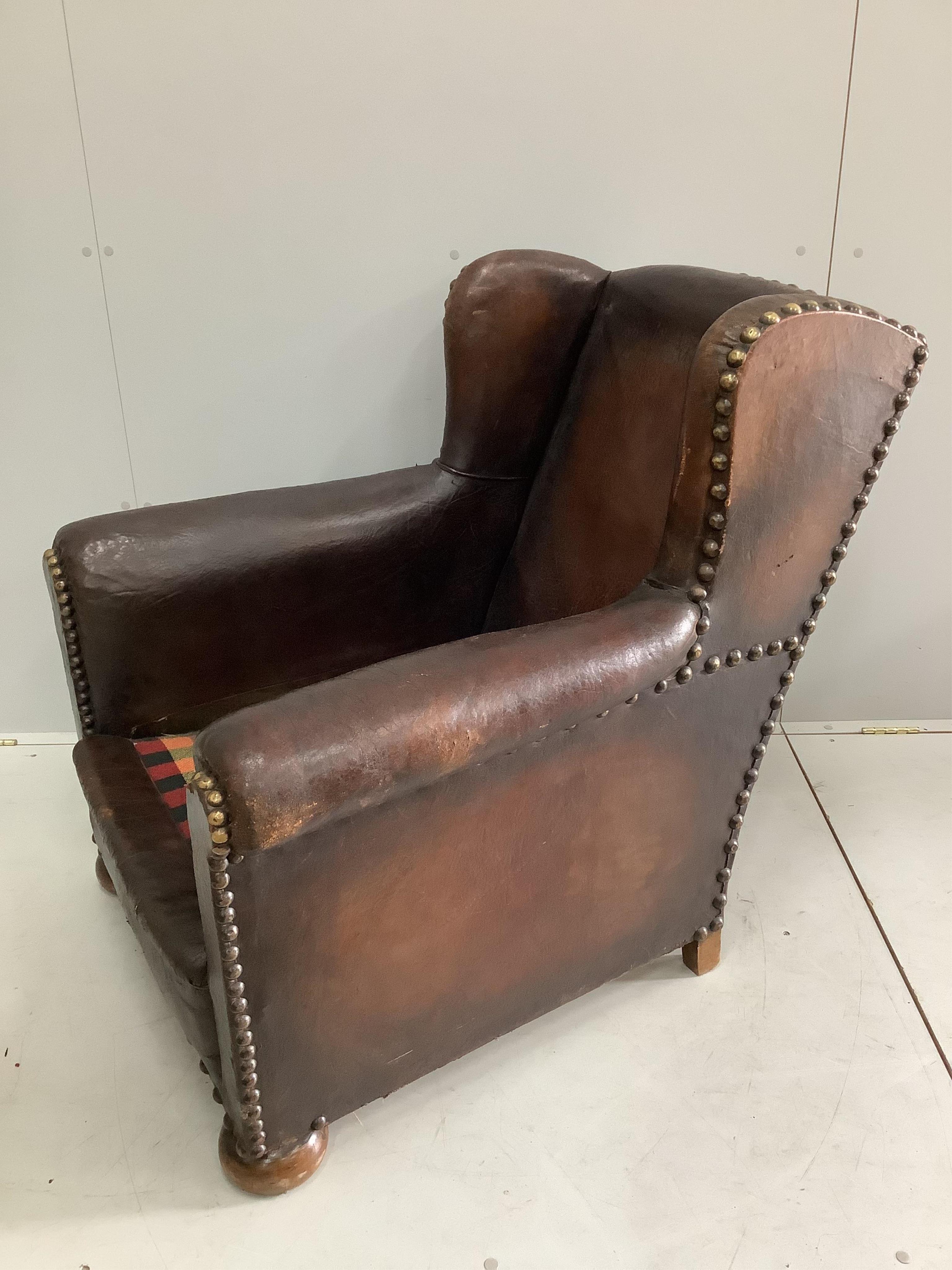 An early 20th century studded tan leather club armchair, width 84cm, depth 90cm, height 92cm. Condition - fair